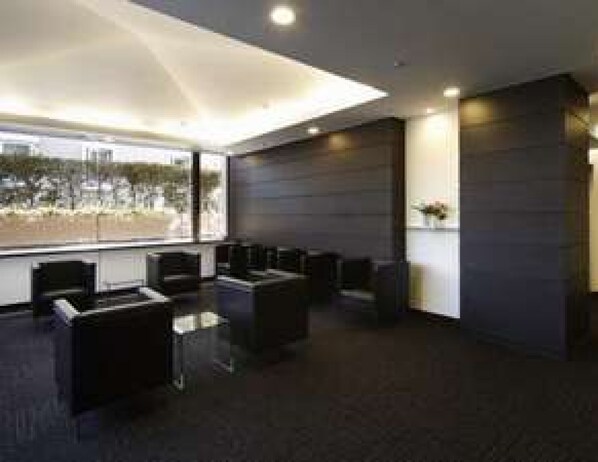 A modern hotel lobby with a seating area, a large window with a view, and a dark-colored reception desk.