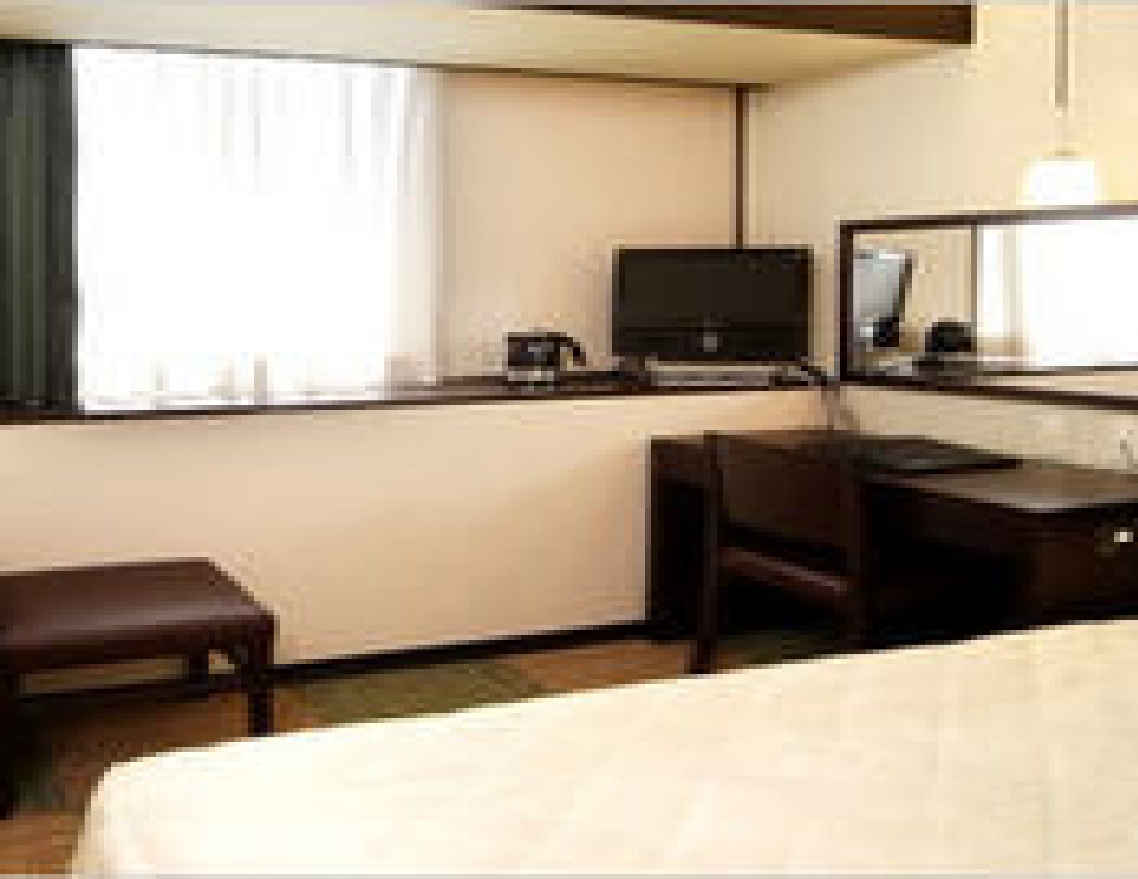 Habitación de hotel con cama, escritorio, computadora, silla, una mesita y ventana con cortinas.