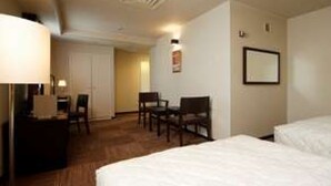 A hotel room with a bed, a desk with a lamp, two chairs, and a framed picture on the wall.