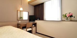 Quarto de hotel com cama, escrivaninha, cadeira, televisão, janela com cortinas e um vaso com flores.