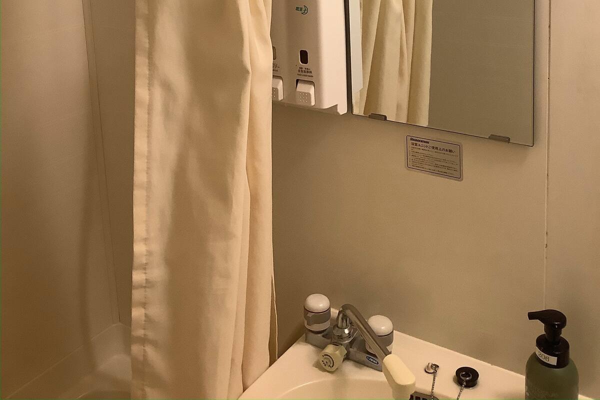 A bathroom with a shower curtain, a mirror, a sink with a soap dispenser, and a towel rack.