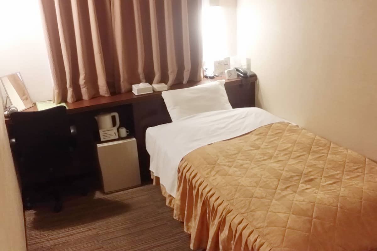 A hotel room with a bed, a desk with a coffee maker, a telephone, and curtains.