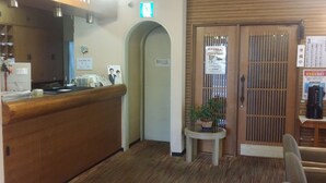 A reception area with a wooden counter, a small table with a potted plant, and a door with a sign. - Hotel Onahama Hills (Iwaki)