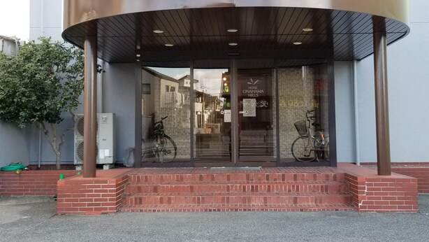 A hotel entrance with a curved metal canopy, glass doors, and a brick base. - Hotel Onahama Hills (Iwaki)