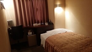 A hotel room with a bed, a desk with a chair, a nightstand, a lamp, and a window with curtains. - Hotel Onahama Hills (Iwaki)