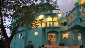 Un edificio turquesa con varios balcones, una escalera que lleva a la entrada y unidades de aire acondicionado.