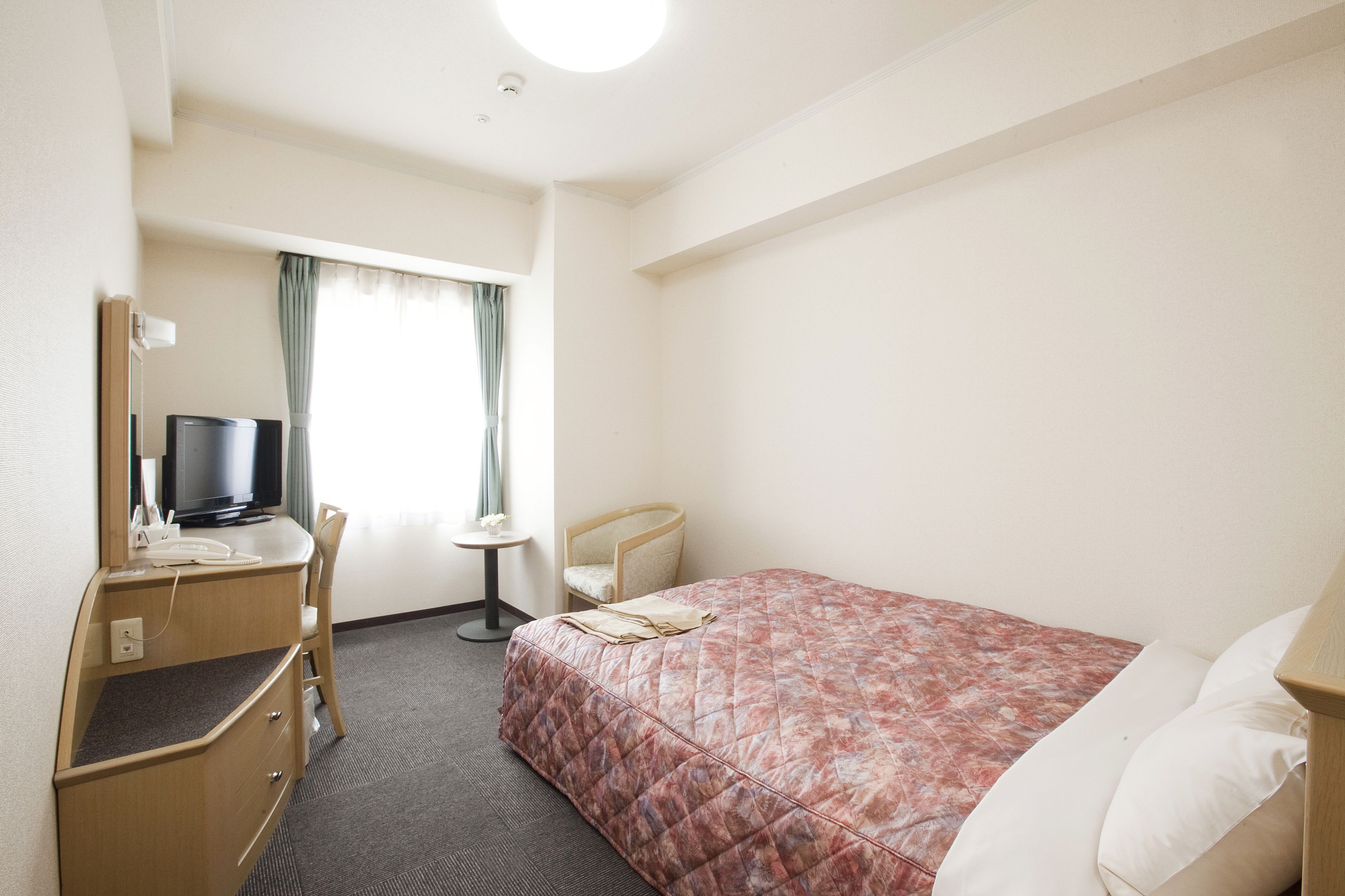 Una camera d'albergo con un letto, una scrivania con una sedia, una televisione e un tavolino.
