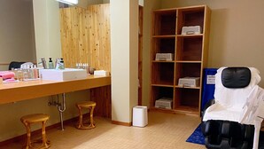 A bathroom with a wooden vanity, stools, a shelf with toiletries, and a massage chair. - Oustat International Hotel Tajimi (Tajimi)