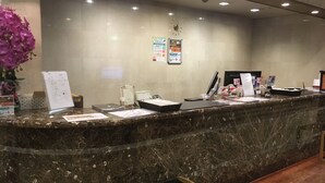 A marble reception desk with a clock, informational posters, and a vase of purple flowers. - Oustat International Hotel Tajimi (Tajimi)