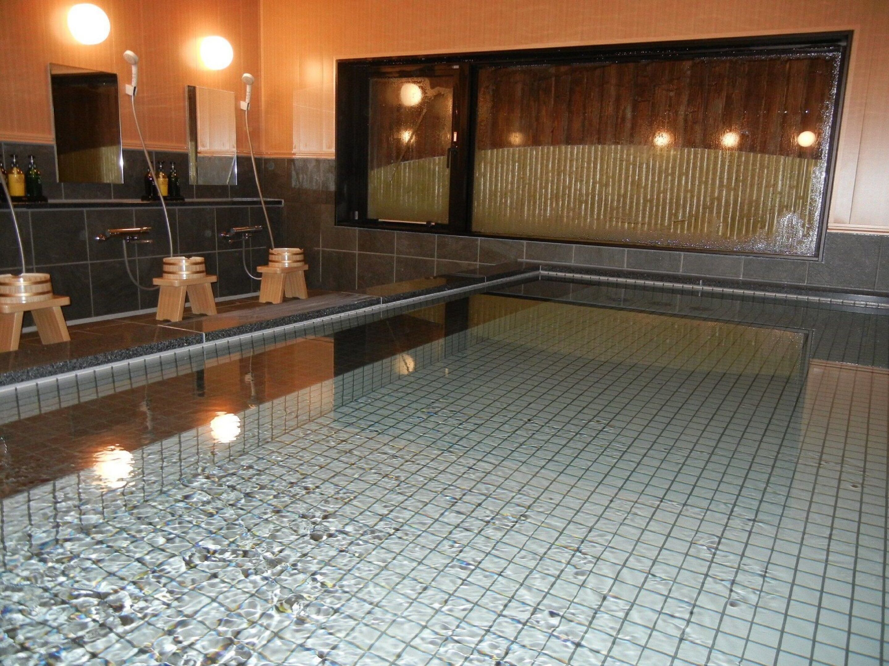 A swimming pool with a tiled floor, wooden stools, and a window with a view.