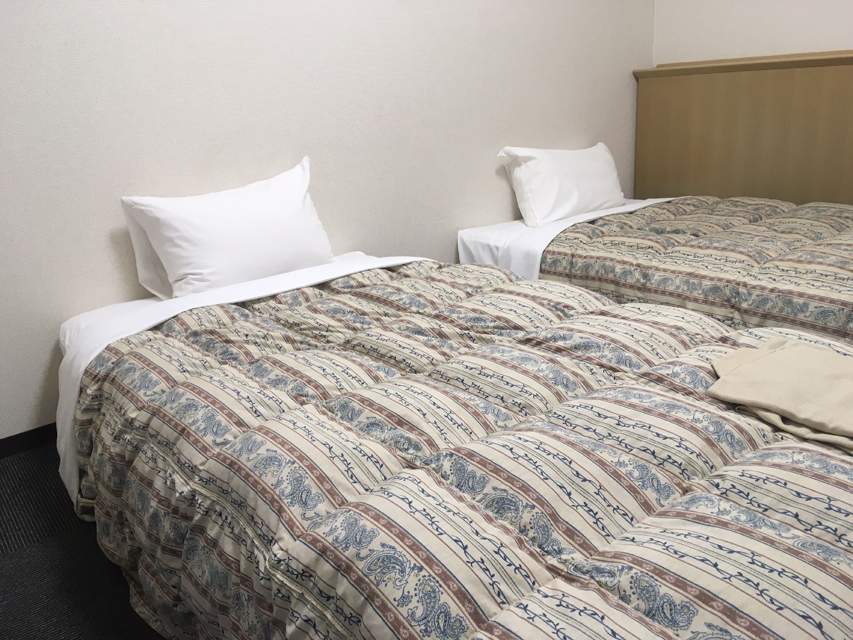 A hotel room with two beds, each with patterned bedding and white pillows.