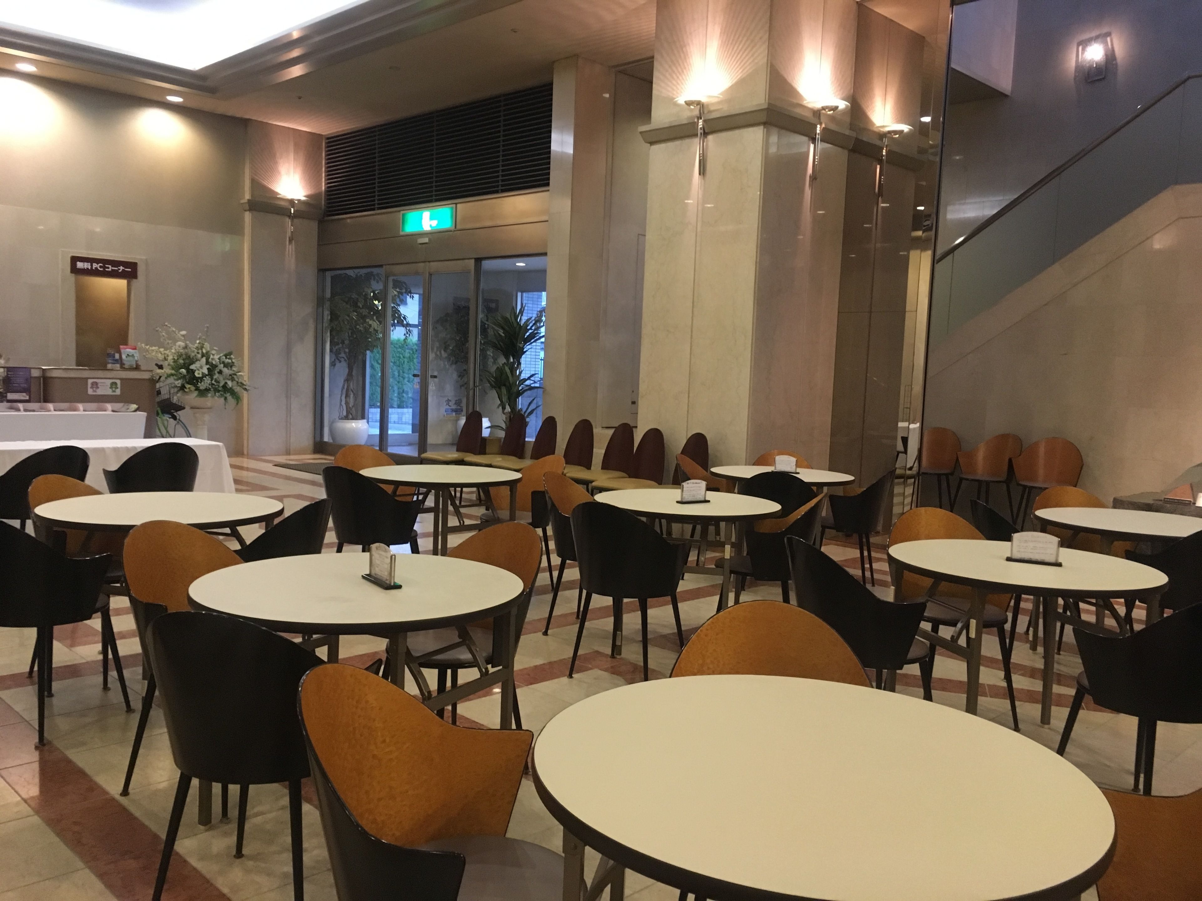 A hotel lobby with round tables and chairs, a reception desk, and a staircase.