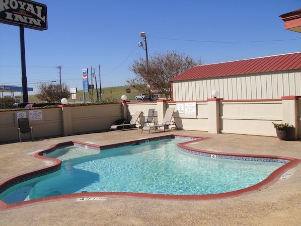 A pool area with a sign for the Royal Inn, a Chevron gas station in the background, and a no diving warning sign.