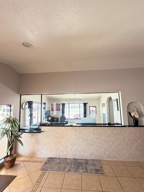 A hotel lobby with a large mirror reflecting the interior, a reception desk, a potted plant, and a tiled floor. - Royal Inn Pearsall (Pearsall)