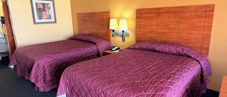 A hotel room with two beds, a wooden headboard, a wall-mounted lamp, and a framed picture.