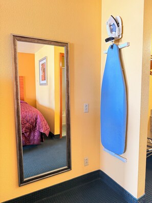 A room with a large mirror, a blue ironing board, and a bed with a patterned blanket. - Royal Inn Pearsall (Pearsall)