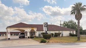A motel with a single-story structure, a covered parking area, and a palm tree in the foreground.