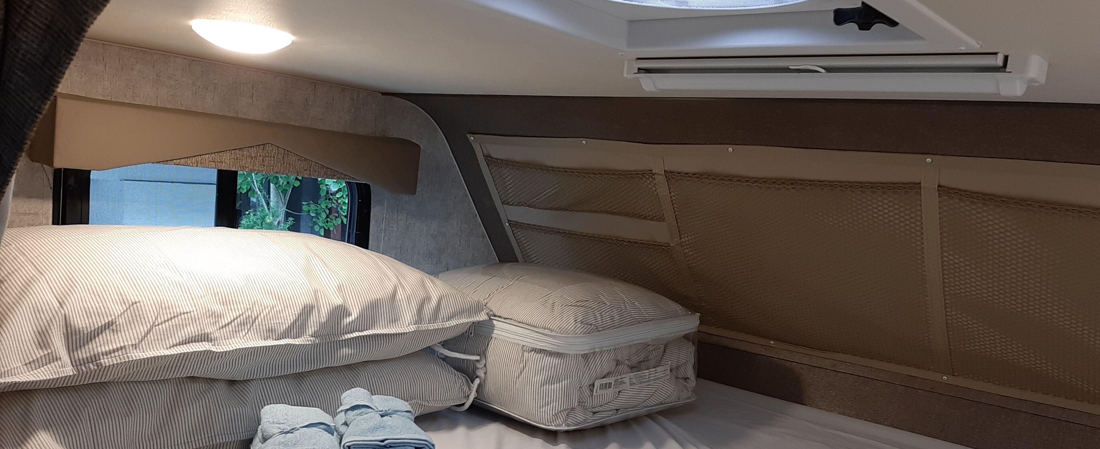 Une pièce compacte et bien éclairée, équipée d’un lit superposé, d’une fenêtre donnant sur un espace verdoyant et d’un appareil de climatisation.