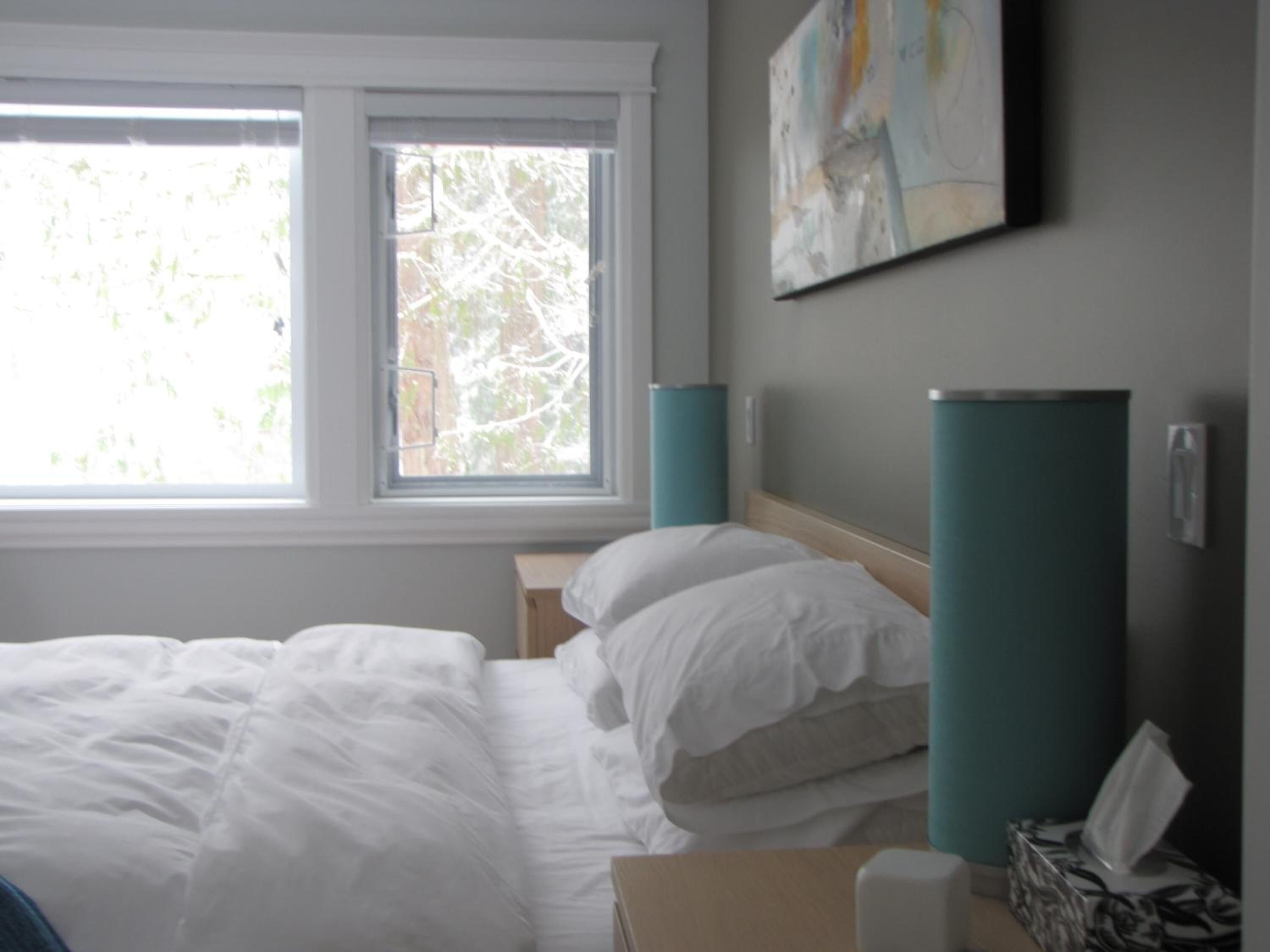 A hotel room with a bed, a window, a wall-mounted artwork, and a bedside table with a tissue box.