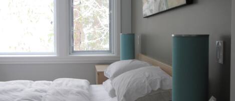 A hotel room with a bed, a window, a wall-mounted artwork, and a bedside table with a tissue box.