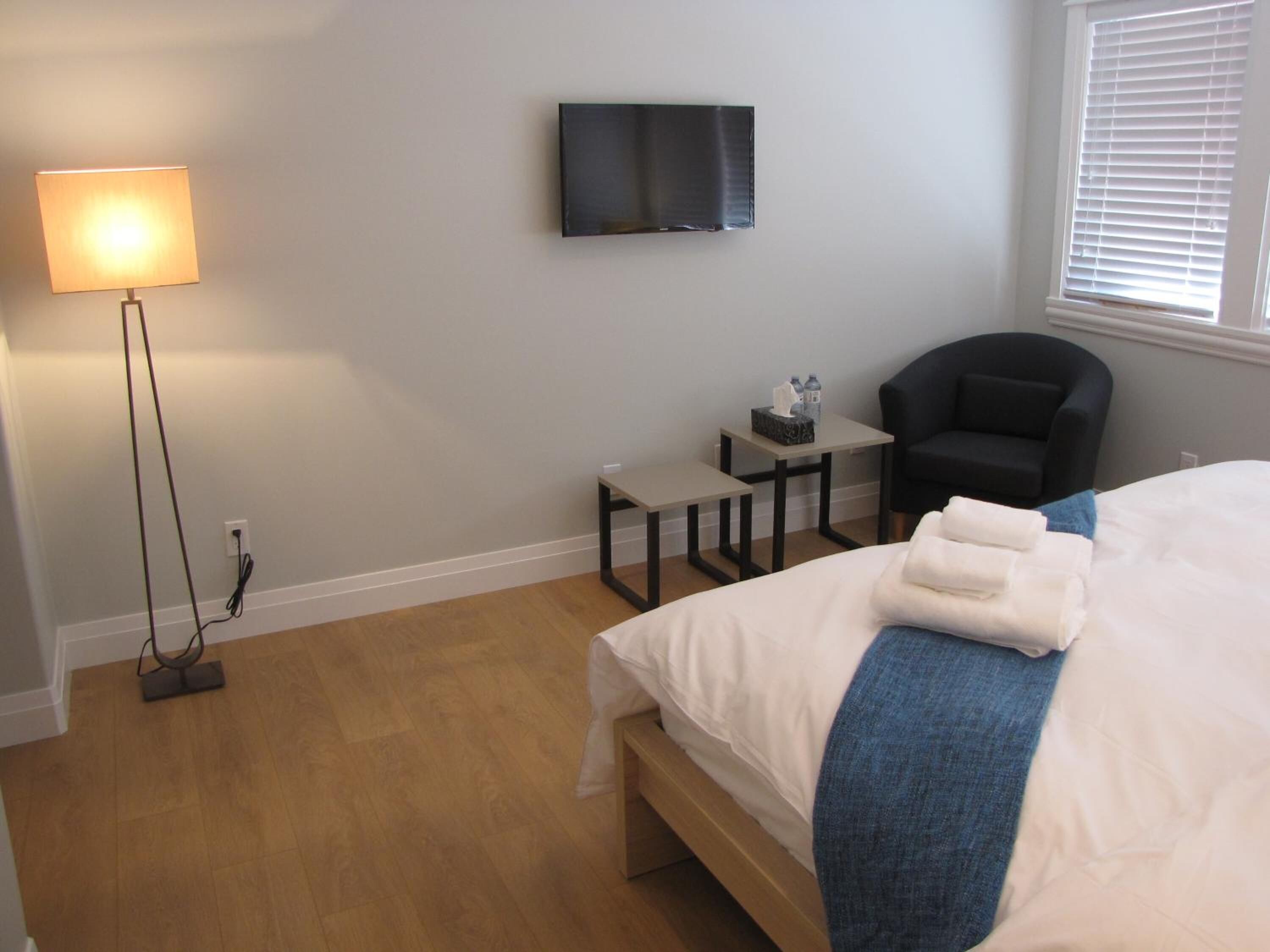 A bedroom with a bed, a desk, a chair, a TV, and a lamp.