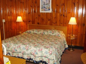 A wooden-paneled room with a bed, two bedside lamps, and a framed picture on the wall. - Black Forest Inn of Adamstown (Adamstown)