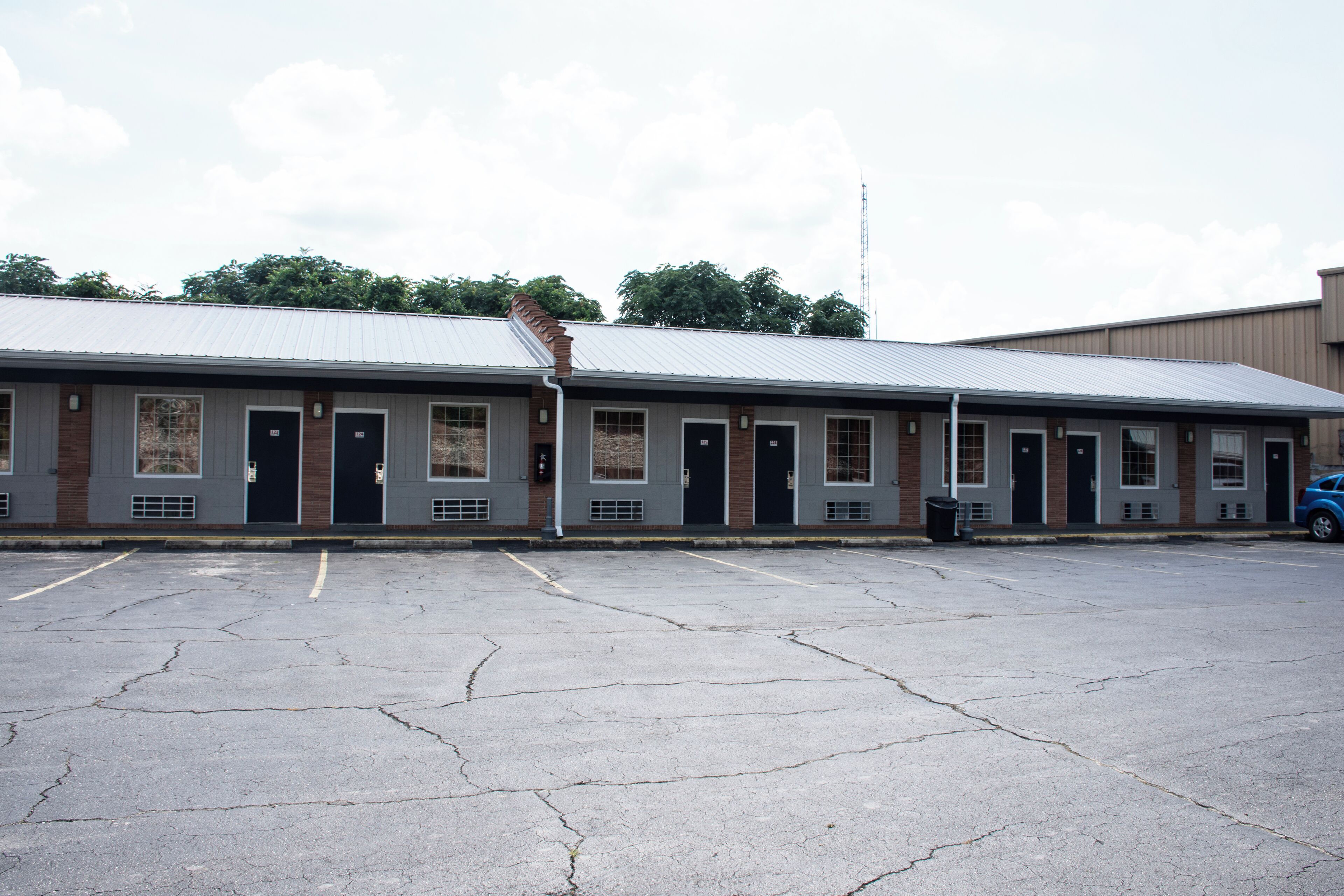 A motel with a row of rooms, a parking lot, and a blue car parked outside.