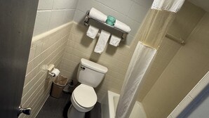 A small bathroom with a toilet, a towel rack with towels, a trash bin, and a shower curtain.