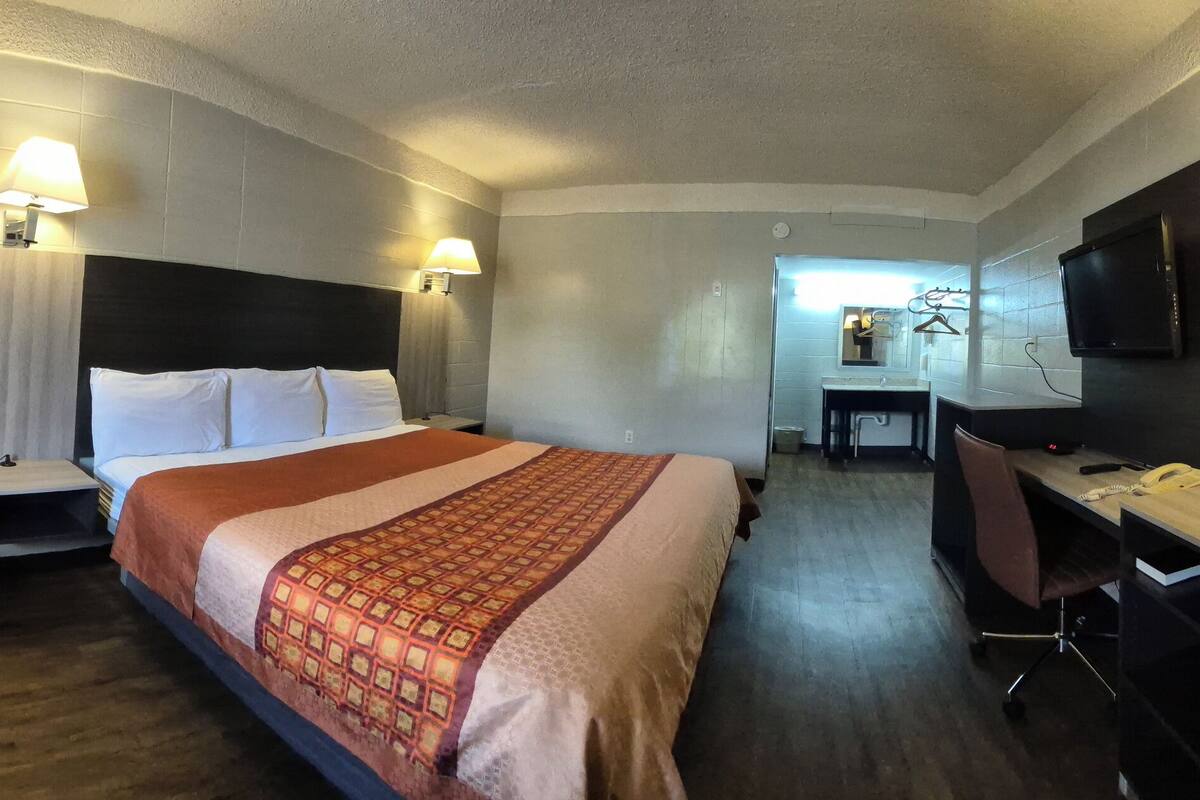 Una habitació d'hotel amb llit, taulells laterals, escriptori amb cadira, televisió i armari.