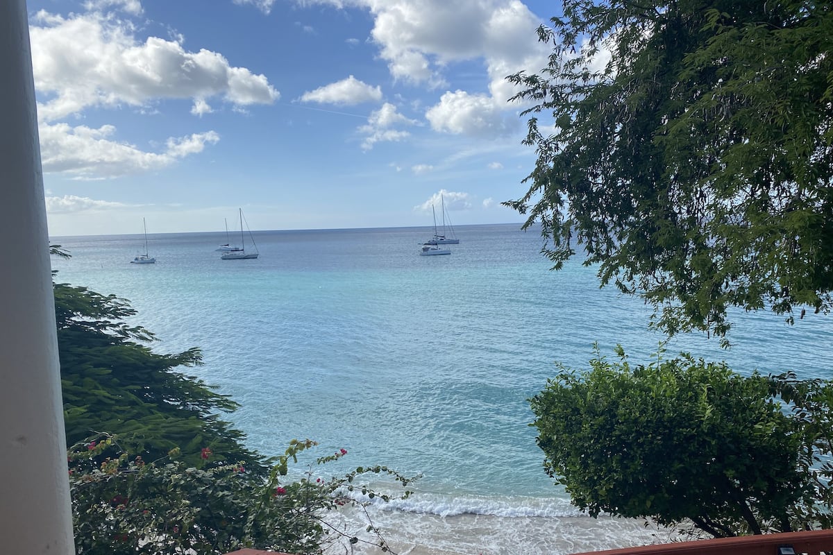 A coastal view with a balcony overlooking the sea, boats, and greenery.
