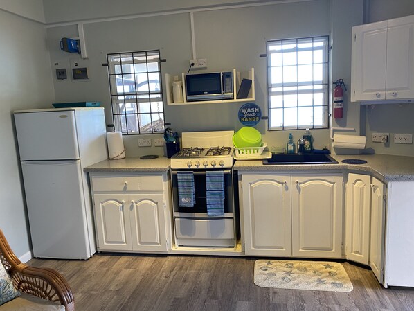 A kitchen with white cabinets, a stove, a microwave, and a refrigerator. - Sea Glass Place (St. George's)