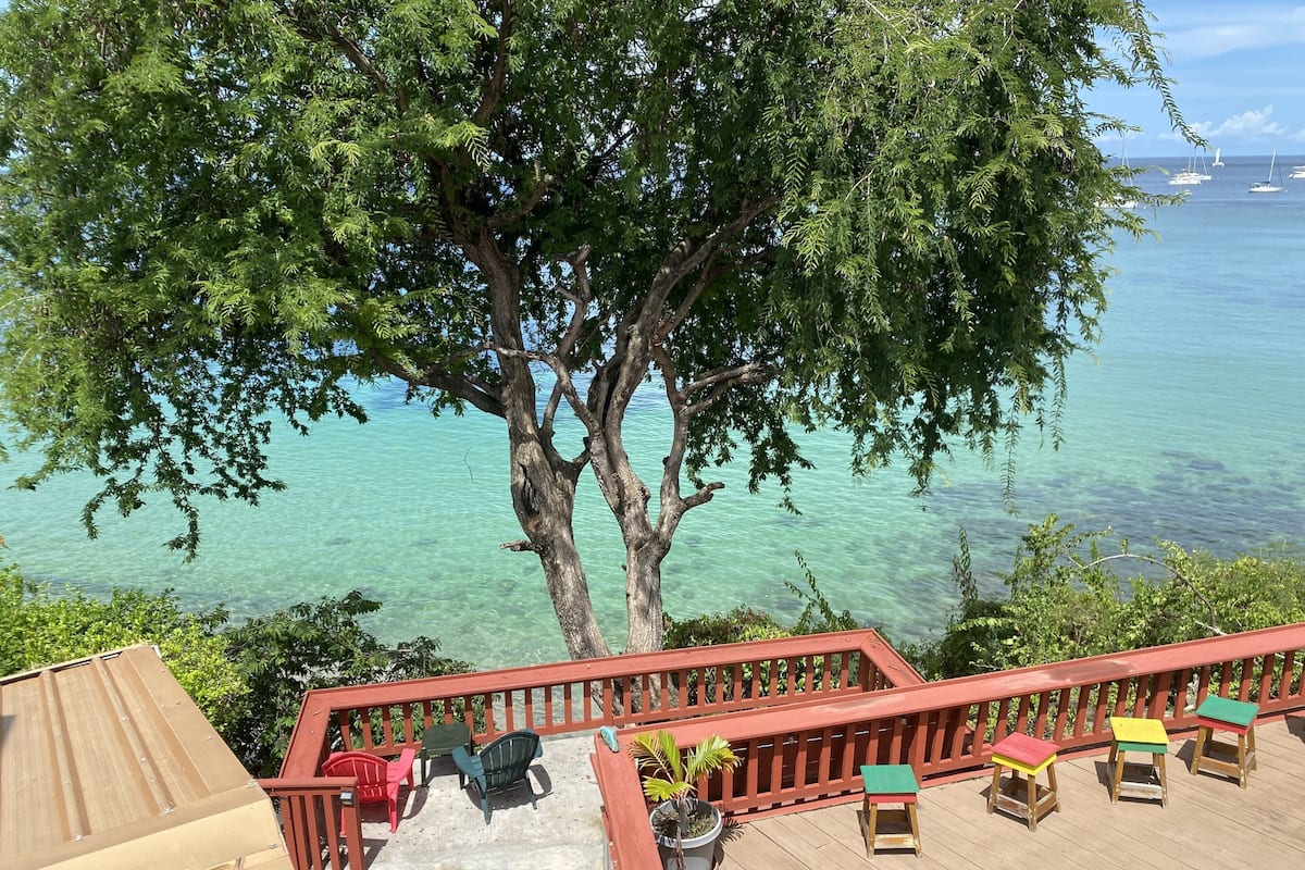 A wooden deck with a red railing, a table with chairs, and a view of the ocean.