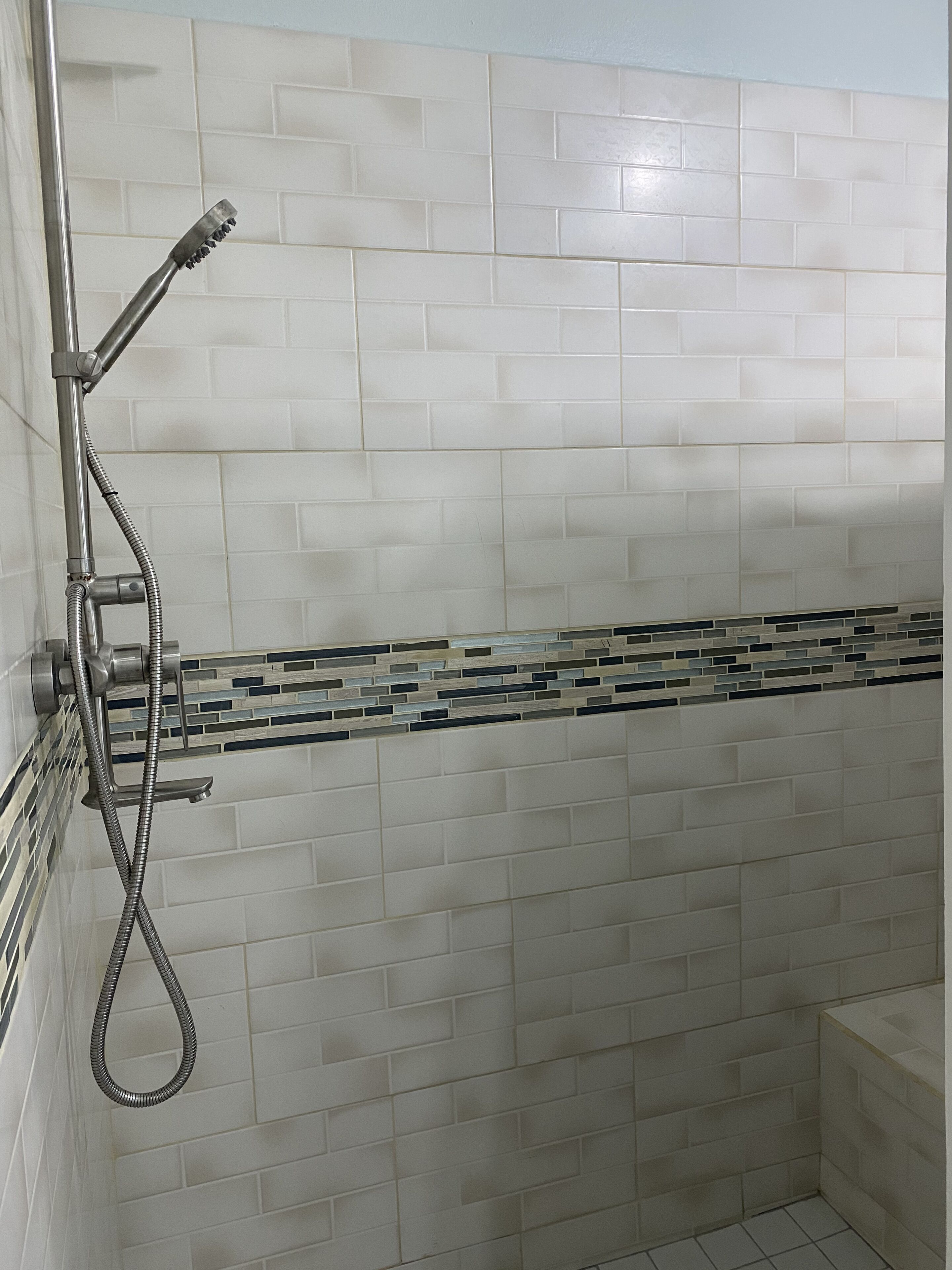 Un área de ducha con pared de azulejos, cabezal de ducha metálico y manguera flexible.