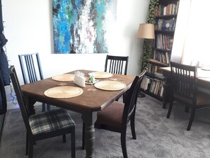 A dining area with a wooden table, four chairs, and a bookshelf filled with books. - Seagrass Guesthouse (Tsawwassen)