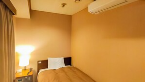 A hotel room with a single bed, a bedside table with a lamp, a telephone, and a wall-mounted air conditioner. - Hotel Takamatsu Hills (Takamatsu)