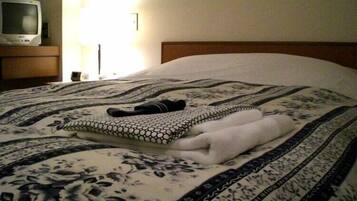 A neatly made bed with a patterned bedspread, a folded towel, and a pair of slippers on the bed.
