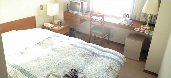 A hotel room with a bed, a desk with a computer, a chair, a lamp, and a television.