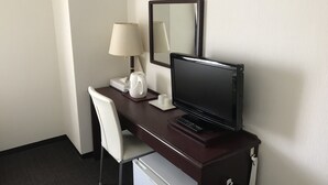 Un bureau dans une chambre d’hôtel, avec un ordinateur, une lampe, un miroir, une chaise et un mini-réfrigérateur.