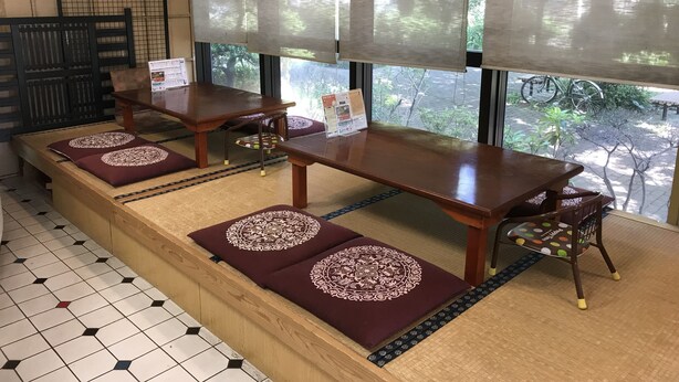 Un restaurant avec des tables et des bancs en bois, un sol carrelé et de grandes fenêtres équipées de stores.