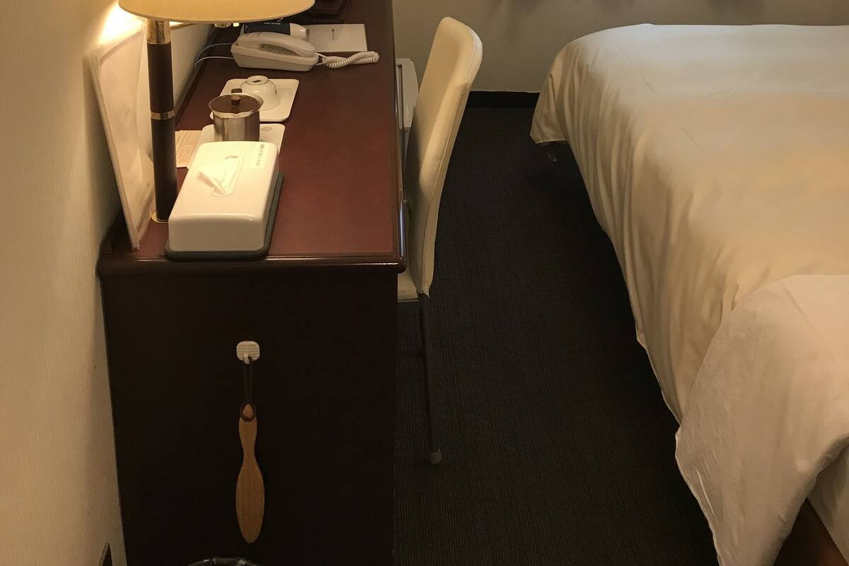 Ein Hotelzimmer mit einem Bett, einem Schreibtisch mit Lampe, einem Telefon und einem Sessel.