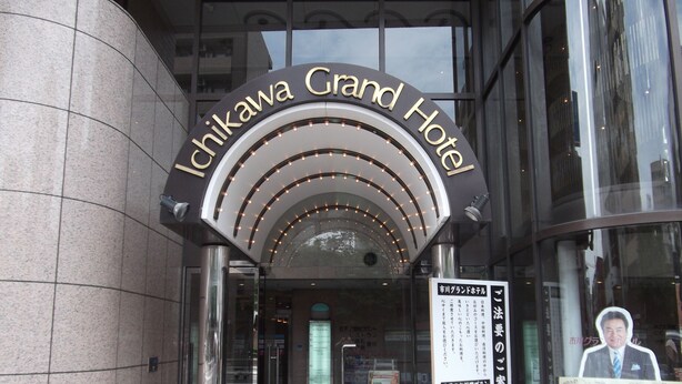 The entrance of the Ichikawa Grand Hotel with a glass door, a red carpet, and a signboard with hotel information. - Ichikawa Grand Hotel (Ichikawa)