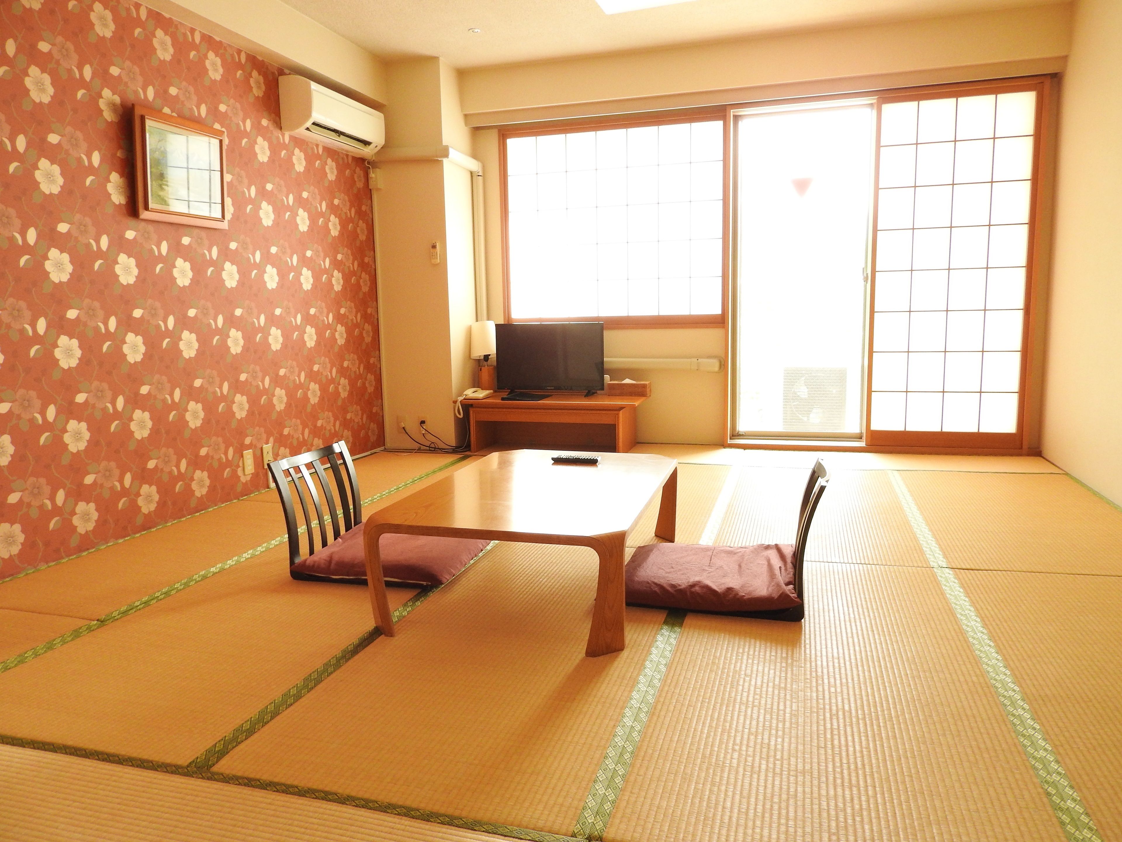 A tatami mat room with a low table, two chairs, a TV, and a sliding door.