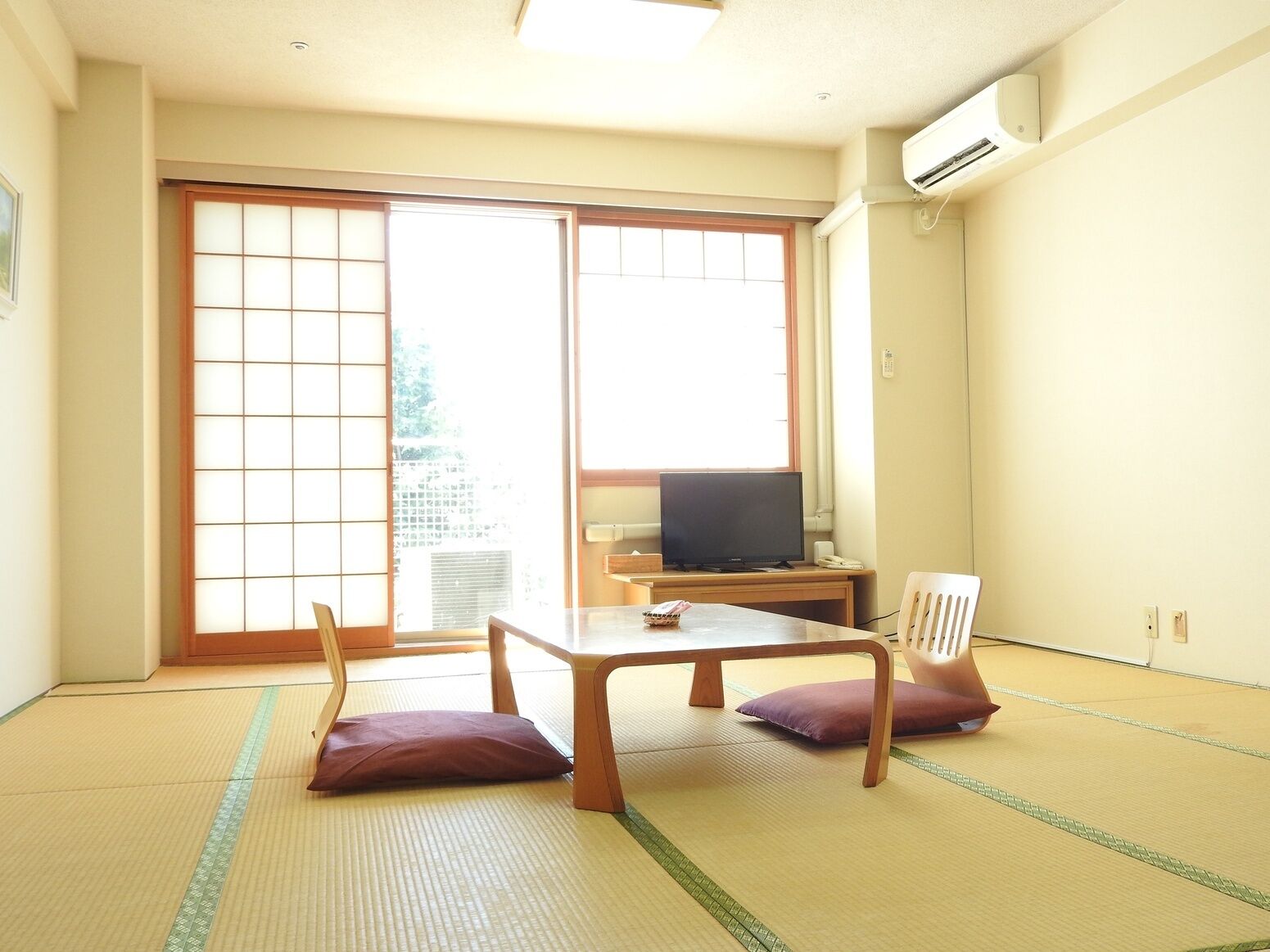 A room with tatami flooring, a television on a wooden table, and sliding doors leading to a balcony.