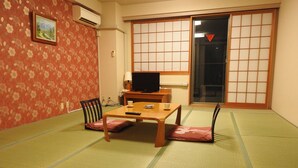 A traditional Japanese room with tatami flooring, a low table with cushions, a television, and a sliding door. - Kai Resort Hotel (Fuefuki)