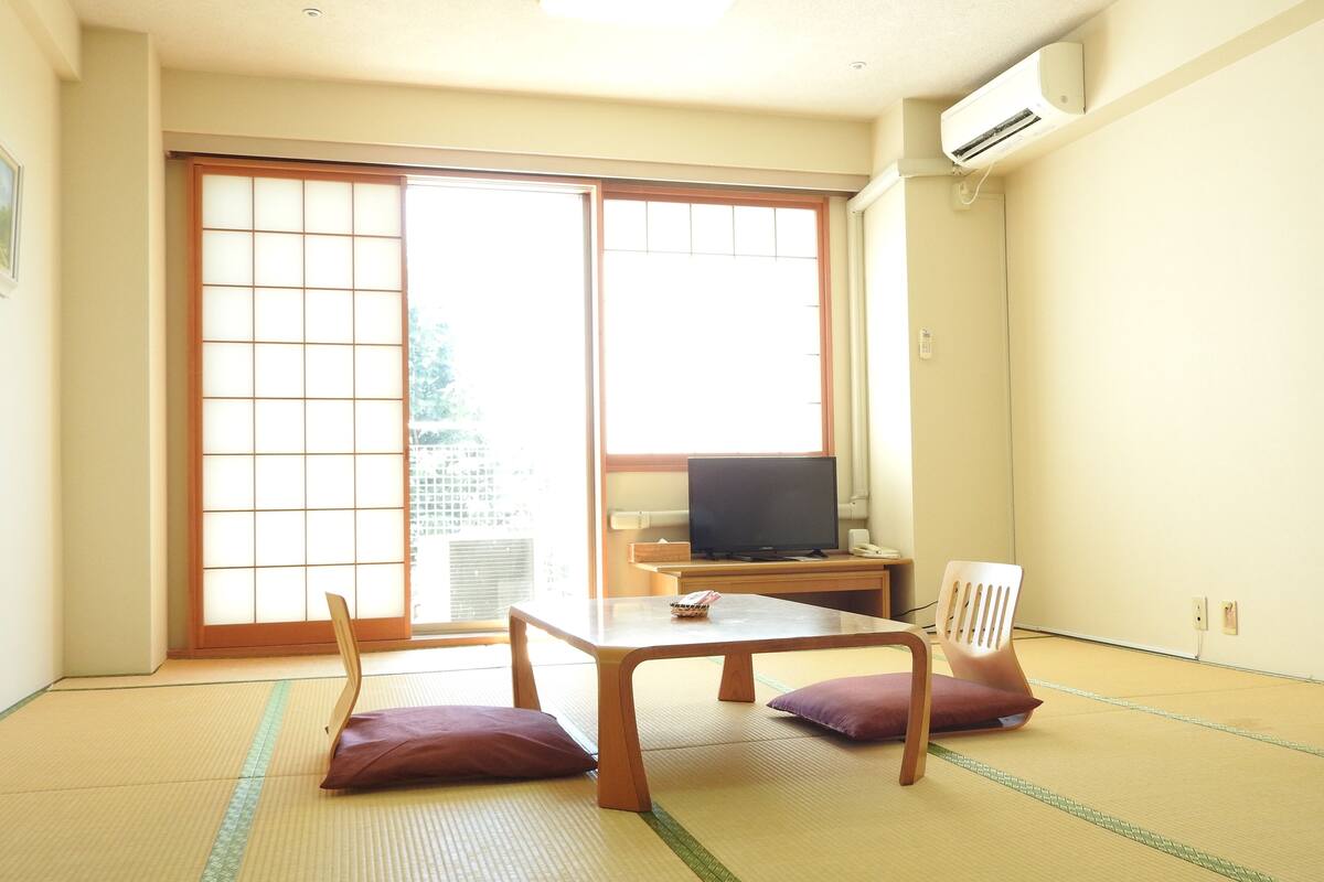 A room with tatami flooring, a television on a wooden stand, and a sliding door leading to an outdoor area.