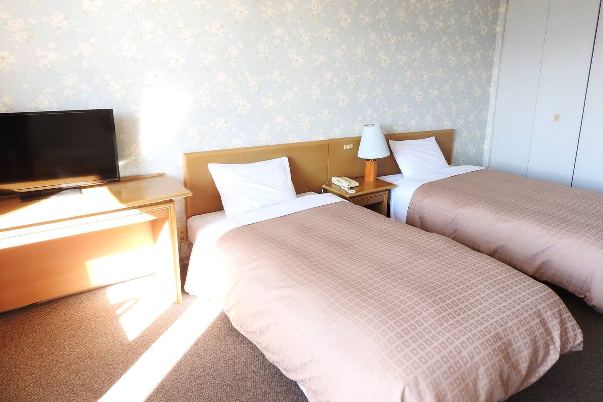A hotel room with two beds, a TV, a desk, and a lamp.