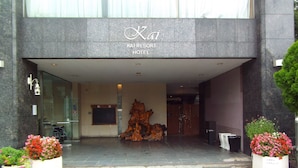 The entrance of Kai Resort Hotel with a modern design, featuring a large wooden sculpture, potted plants, and a tiled pavement. - Kai Resort Hotel (Fuefuki)