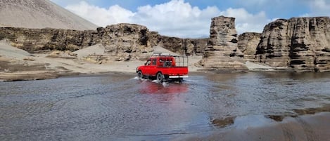 Una camioneta roja circulando por una extensión de agua poco profunda en terreno pedregoso.