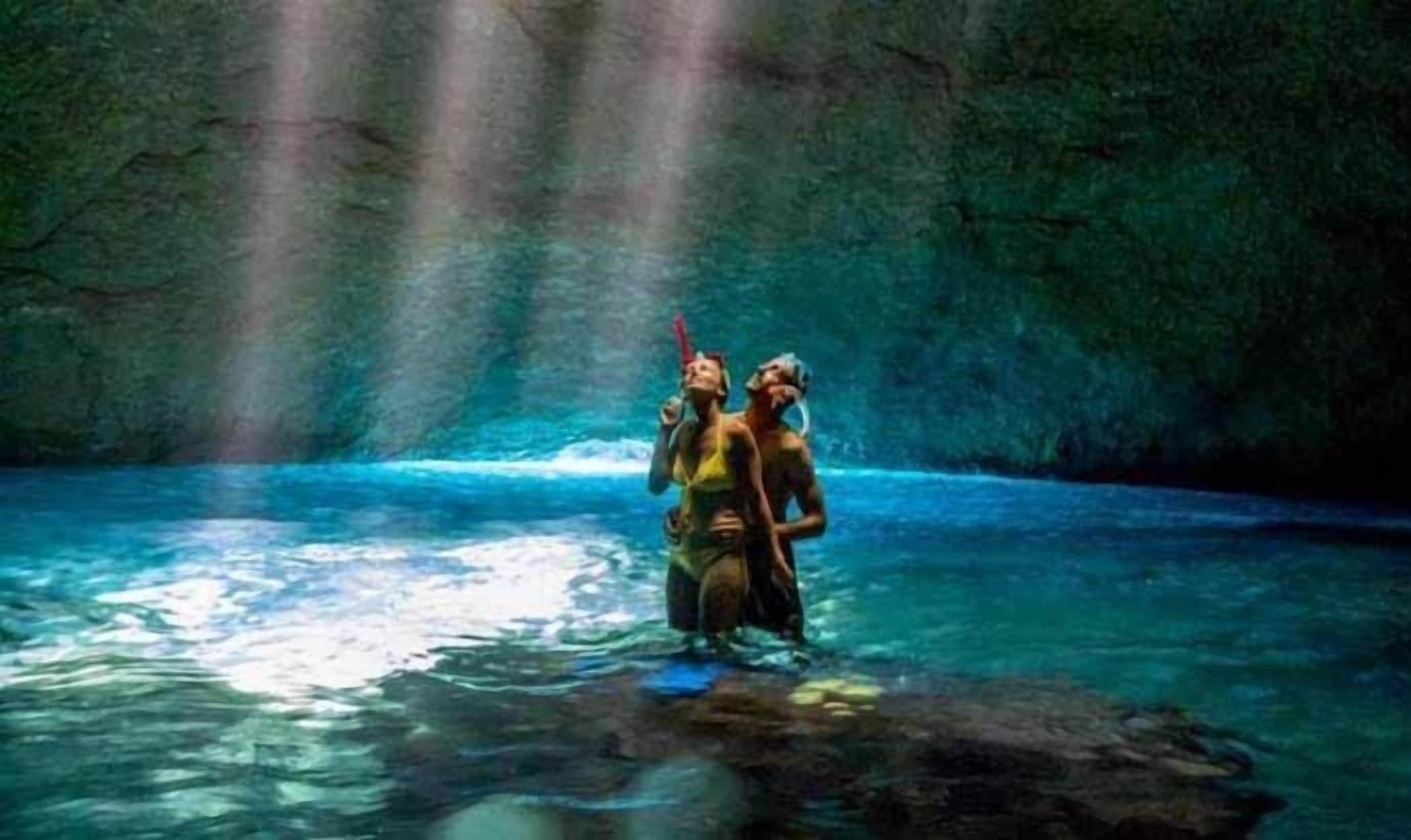 Dos personas haciendo snorkel en una cueva con agua que fluye del techo.
