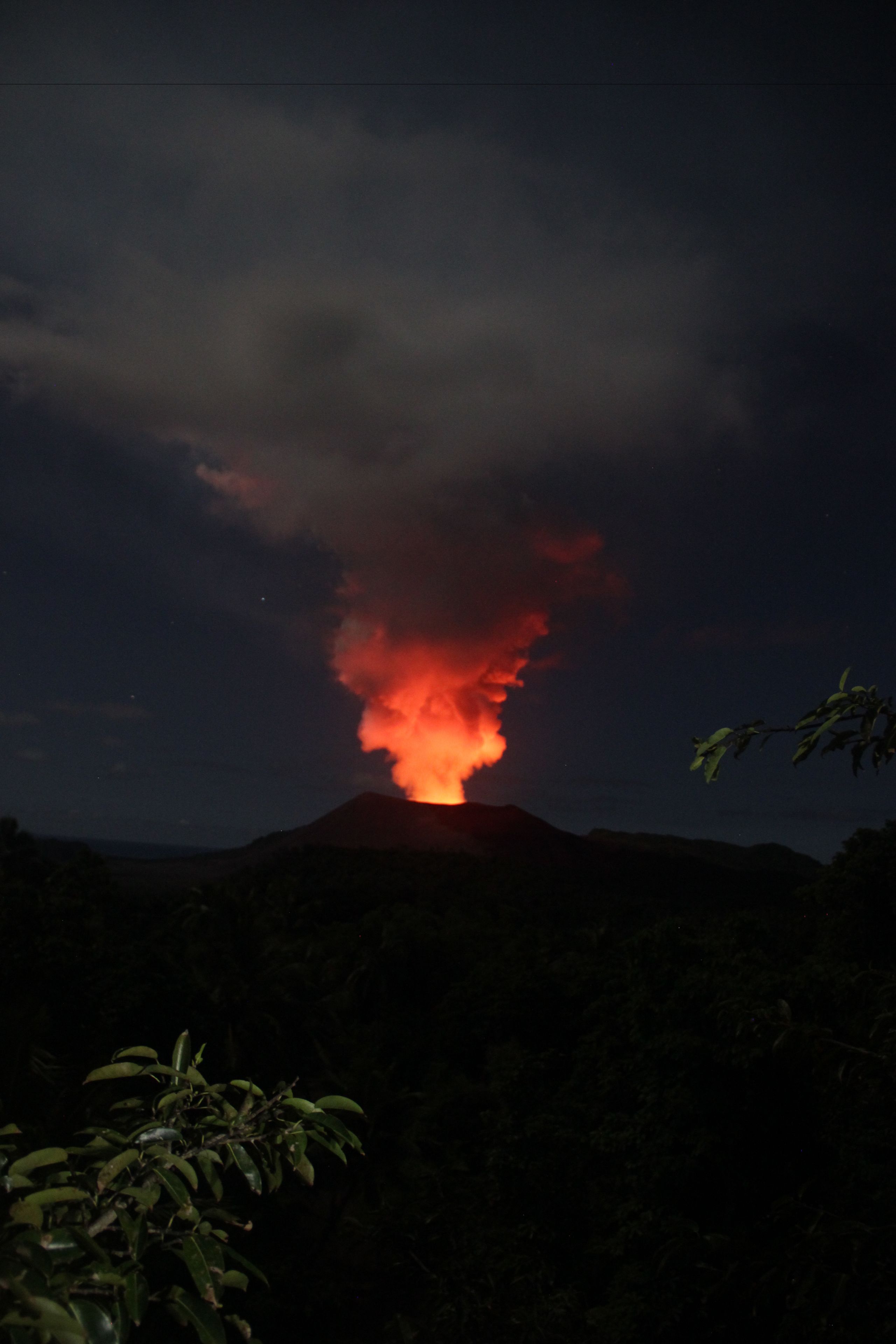 A volcano with a glowing lava plume at night.